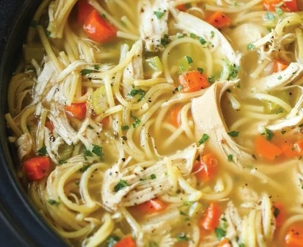Bowl of slow cooker chicken noodle soup with fresh herbs and vegetables