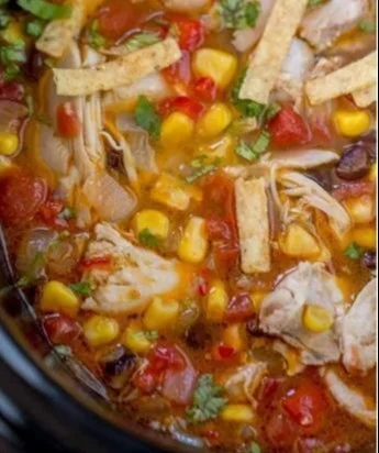 Bowl of slow cooker chicken tortilla soup garnished with tortilla strips and cilantro.