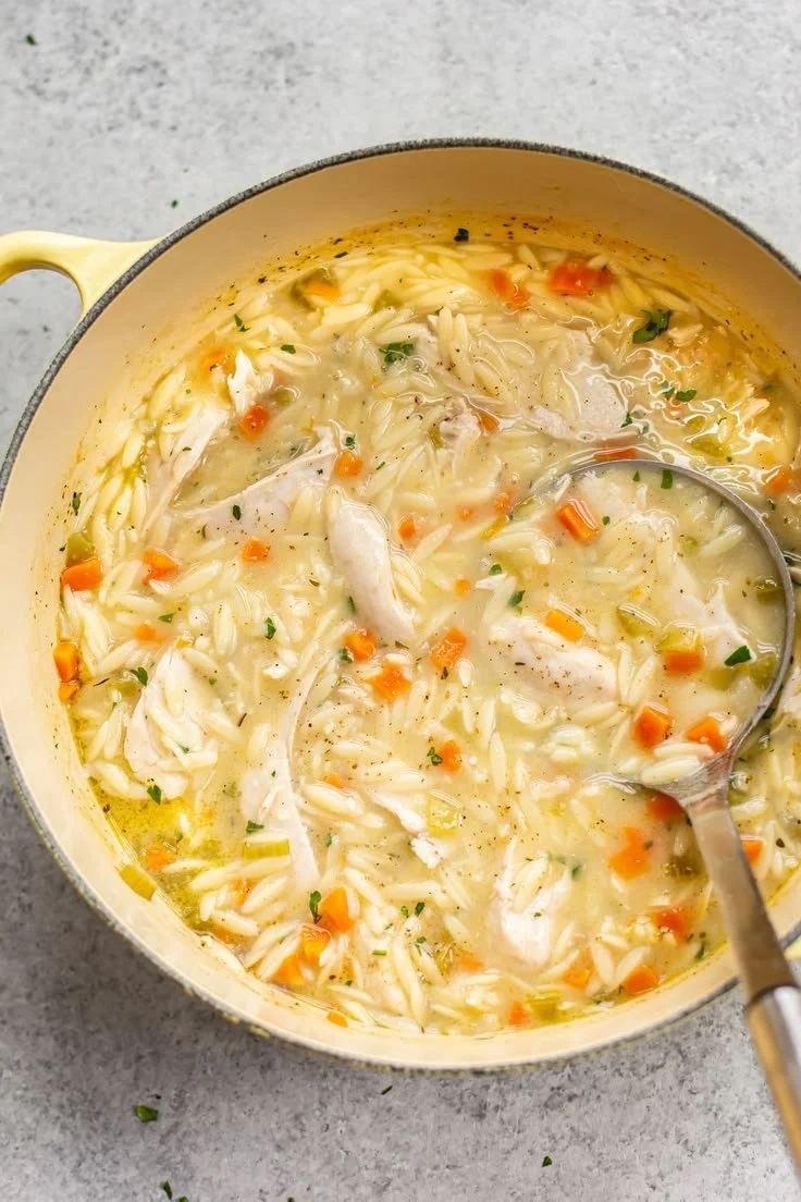 Bowl of lemon chicken orzo soup with fresh herbs and lemon slices